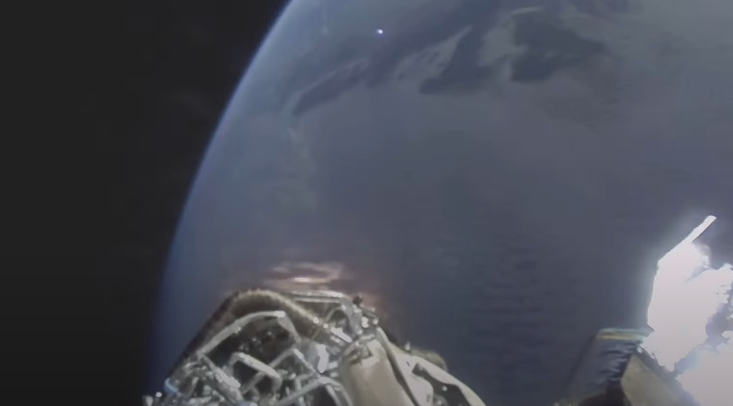 earth can be seen behind metallic tubing and wires on the outside of a spacecraft