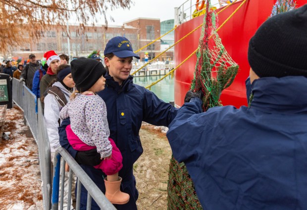 A member of the United States Coast Guard picks up a Christmas tree to load into it into a truck before it was delivered to a local family in need during the 25th Anniversary Voyage of Chicago's Christmas Ship, USCGC Mackinaw, Dec. 6, 2025, at Polk Brothers Park in Chicago. (Dominic Di Palermo/Chicago Tribune)