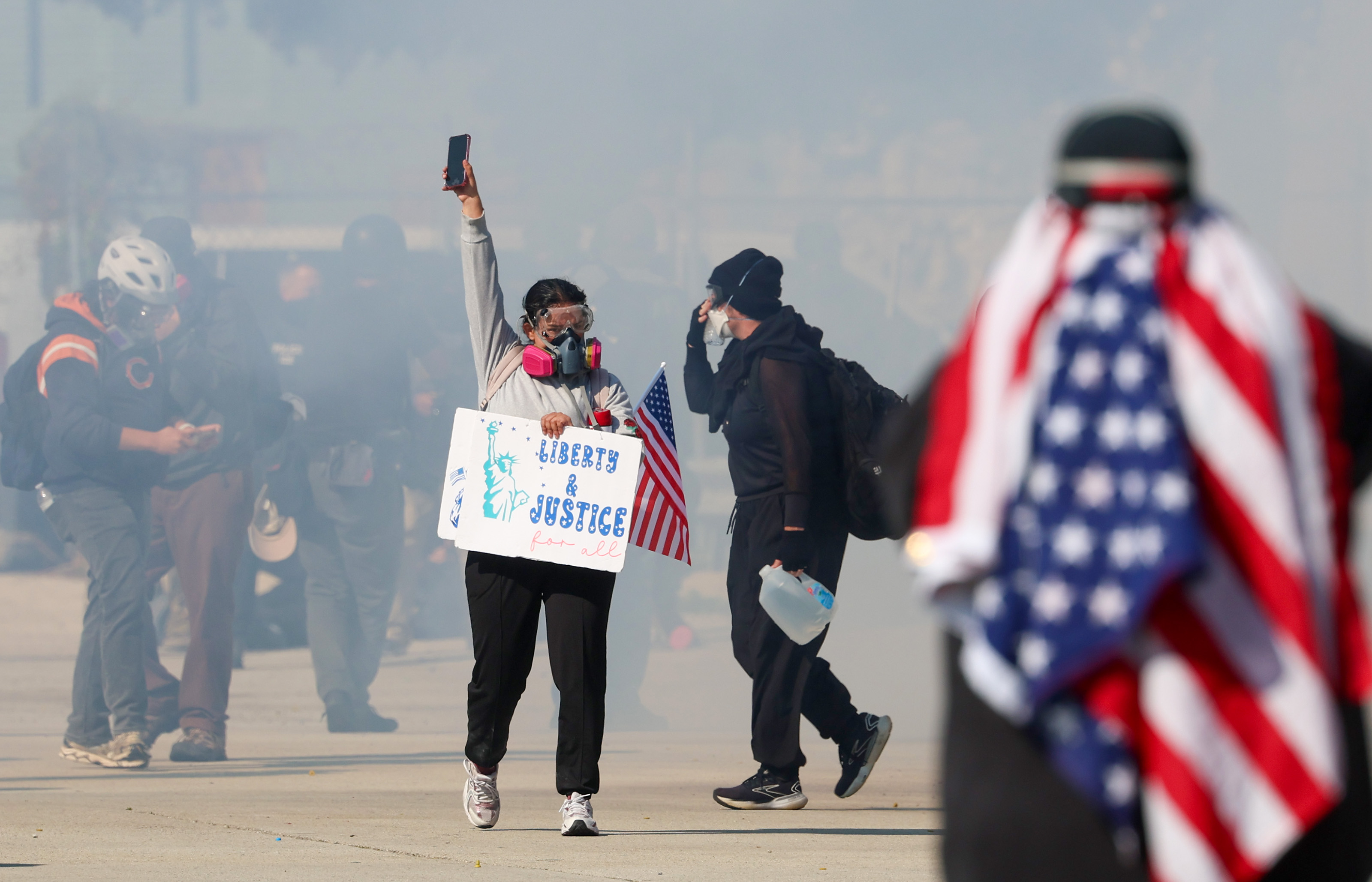 A protester holds up her phone and backs away from...