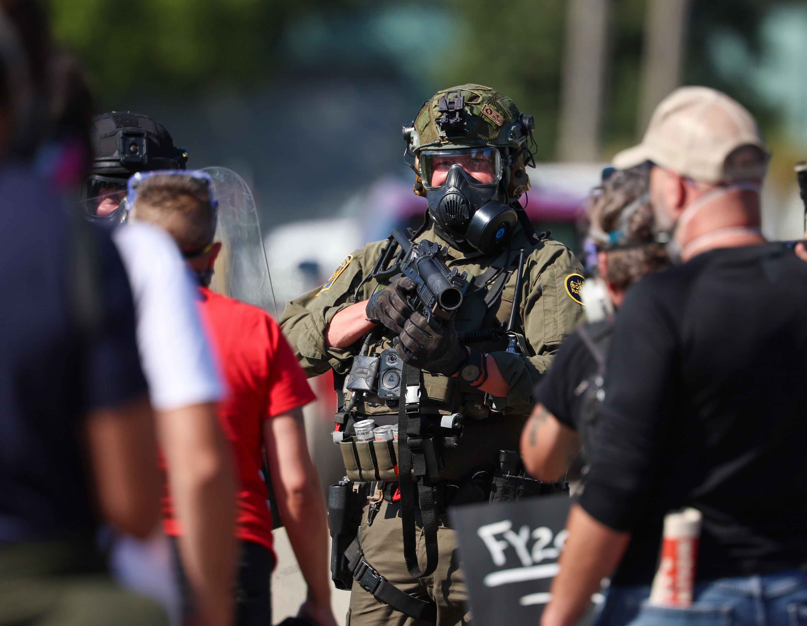 A federal agent points his rifle of pepper balls at...