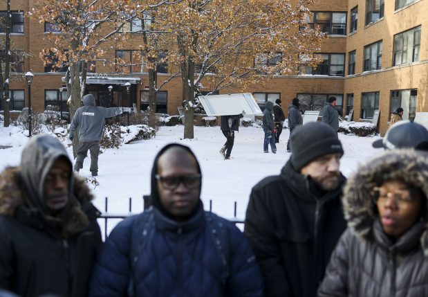 Workers from DAWGS Vacant Property Security bring metal sheets to board up windows while a 7500 South Shore Tenants Union press conference takes place in front of the apartment building in Chicago on Dec. 2, 2025. (Eileen T. Meslar/Chicago Tribune)