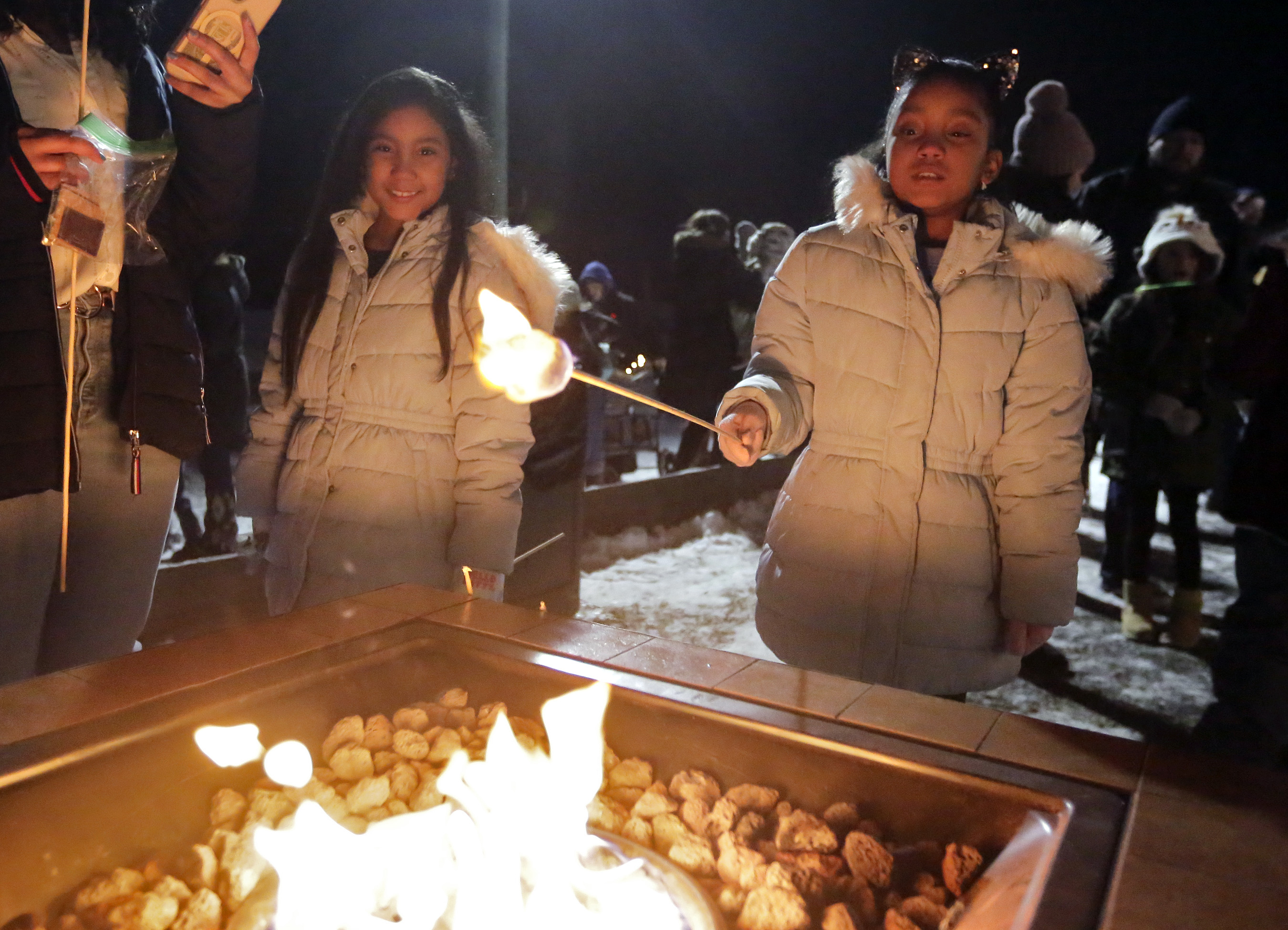 Adeline Perez, 9, right, flames a marshmallow as her twin...