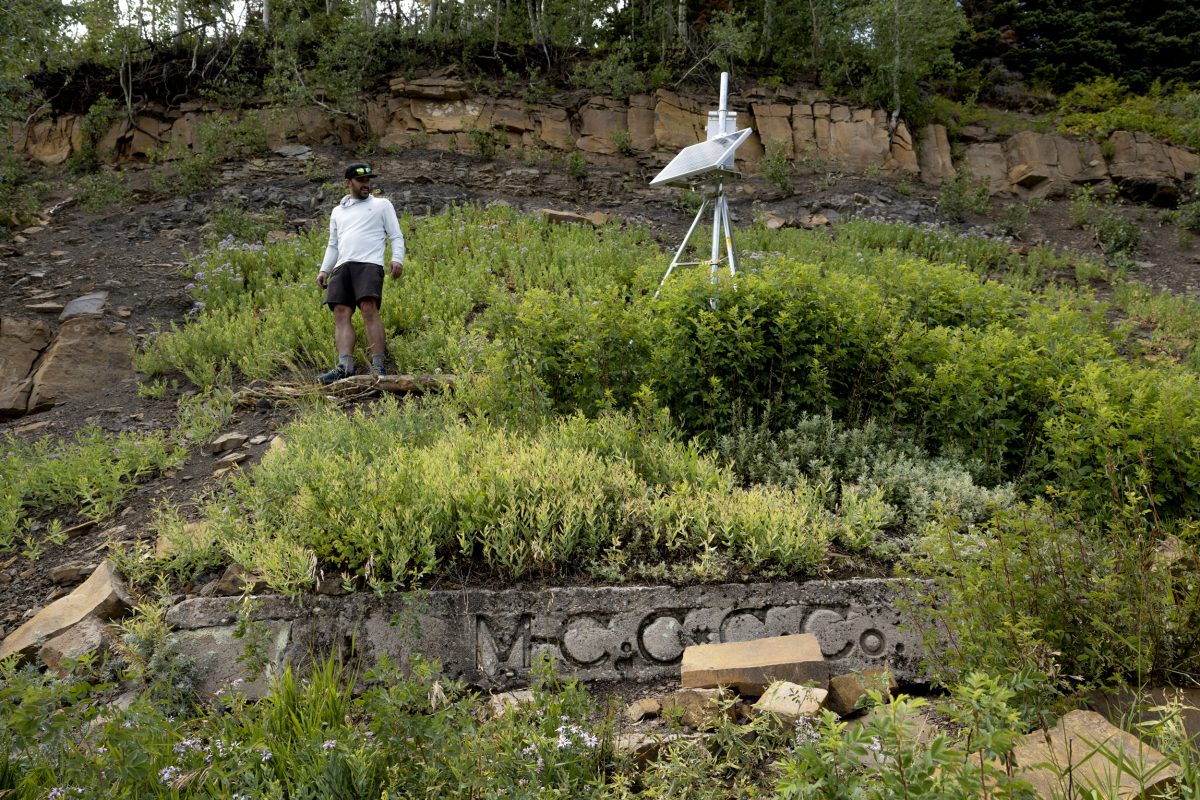 a person standing on a steep hillside looking at a tripod with scientific equipment attached to it