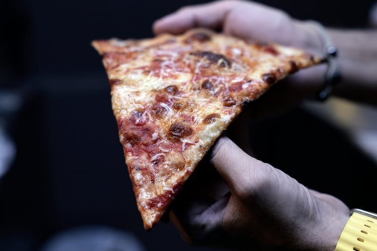 Sebastian Besiso holds a slice of his pizza in his Apizzeria 888 by Sebastian in Elkins Park on Thursday, Nov. 20, 2025.
