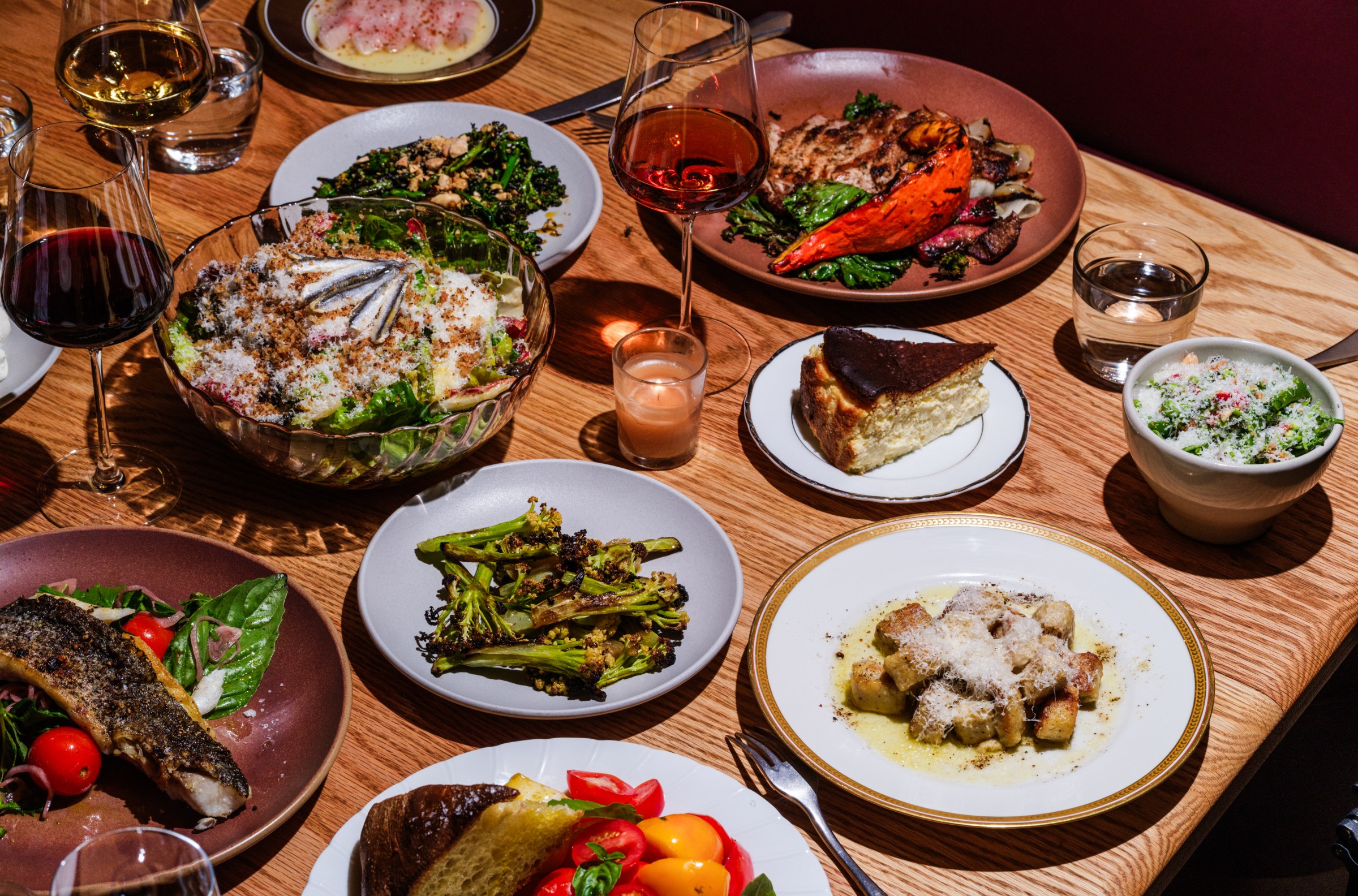 Spread of brightly-lit dishes on a wood table, including salad, broccolini, and more at Betsy.