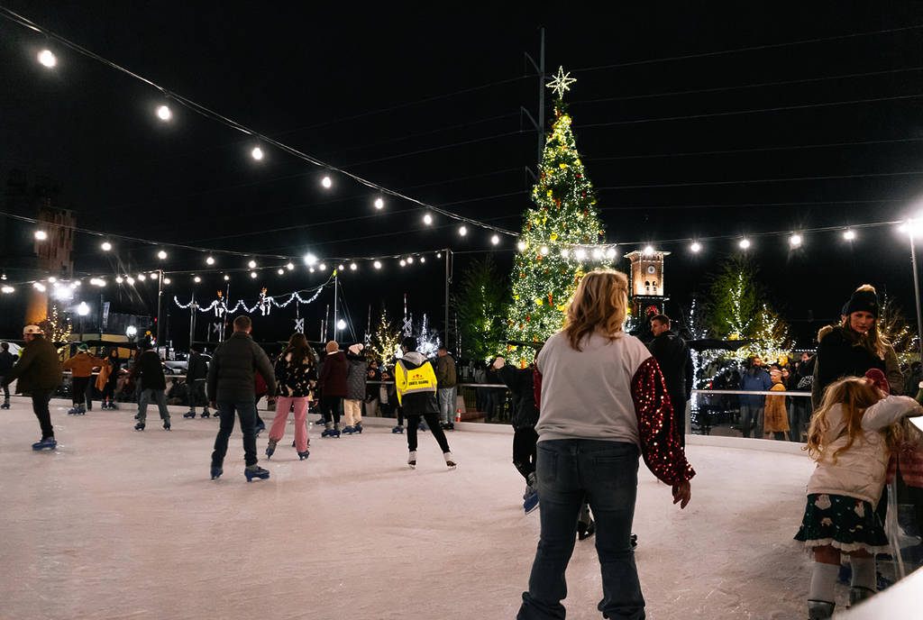 Image shows people skating at the Peace Plaza Ice Rink in Grapevine under lights and the Christmas tree.