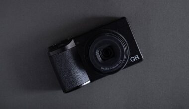 A black compact digital camera with a large lens, labeled "GR," placed on a dark gray surface at a slight angle.