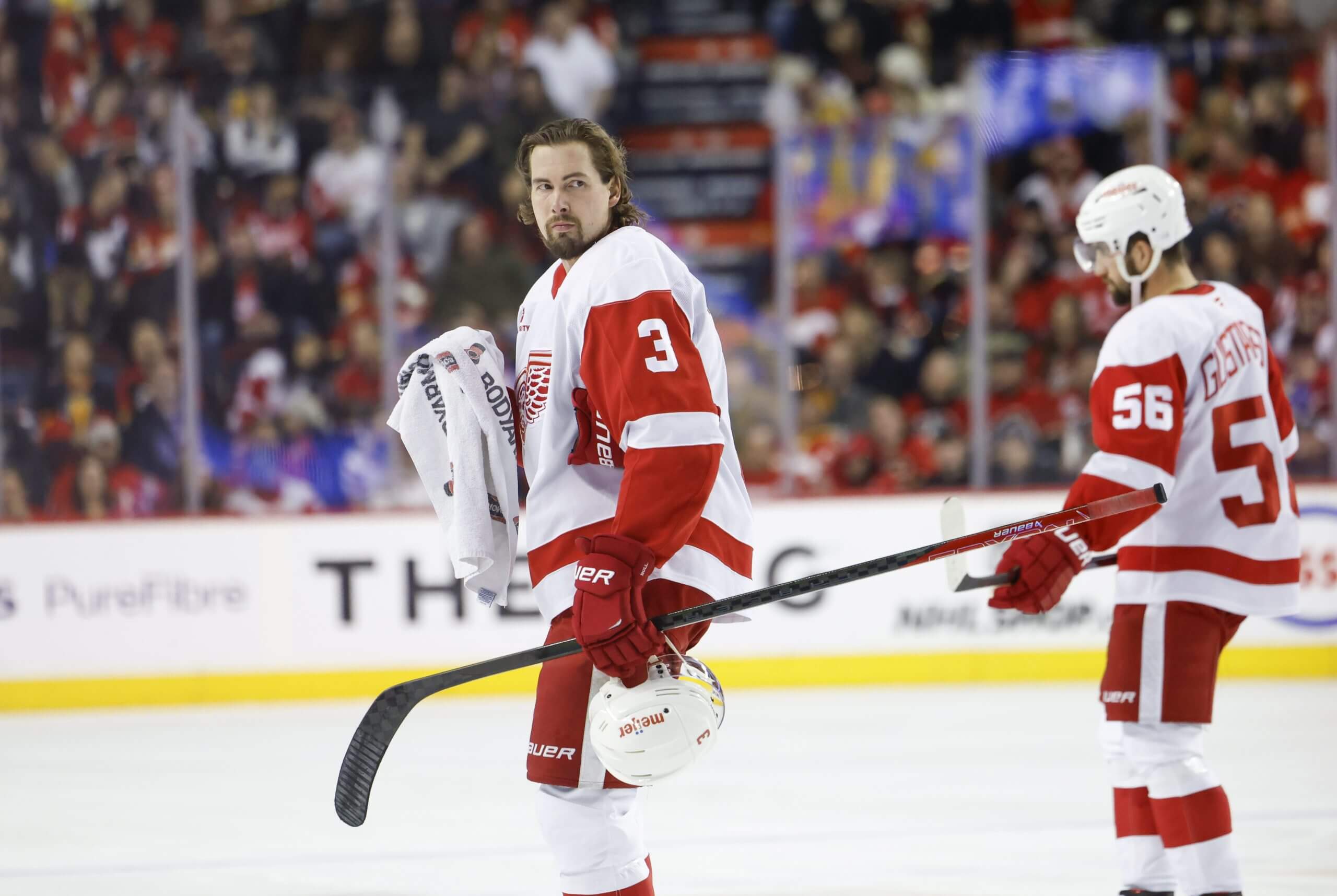 Justin Holl and Erik Gustafsson stand on the ice before a game, with Holl holding his helmet and a towel.
