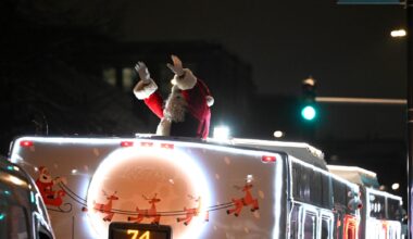 Santa waves from atop a city bus.