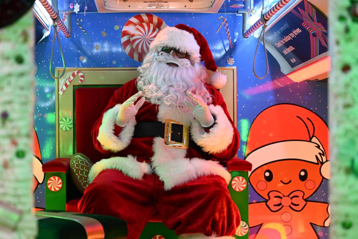 Santa sits in a chair in the back of a bus.