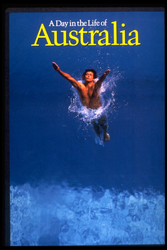 A person swims underwater reaching toward the surface, surrounded by blue water. The text above reads “A Day in the Life of Australia” in white and yellow letters.