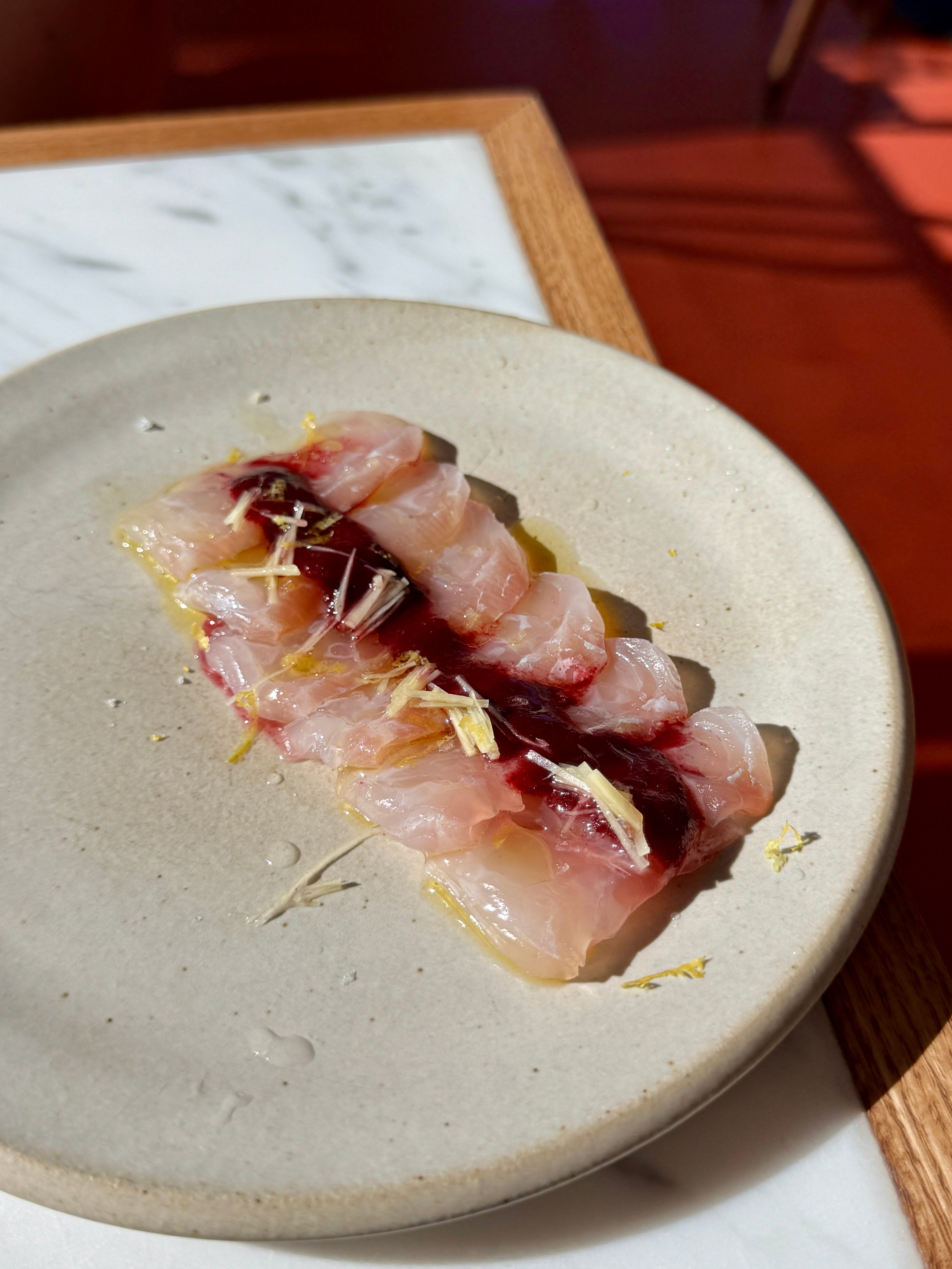 Sliced crudo on a cream-colored plate at Little Fish Melrose Hill.