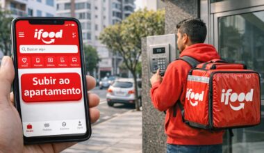 An iFood delivery driver with a red backpack stands in front of a building while a cell phone displays the "Go up to apartment" button on the delivery app.