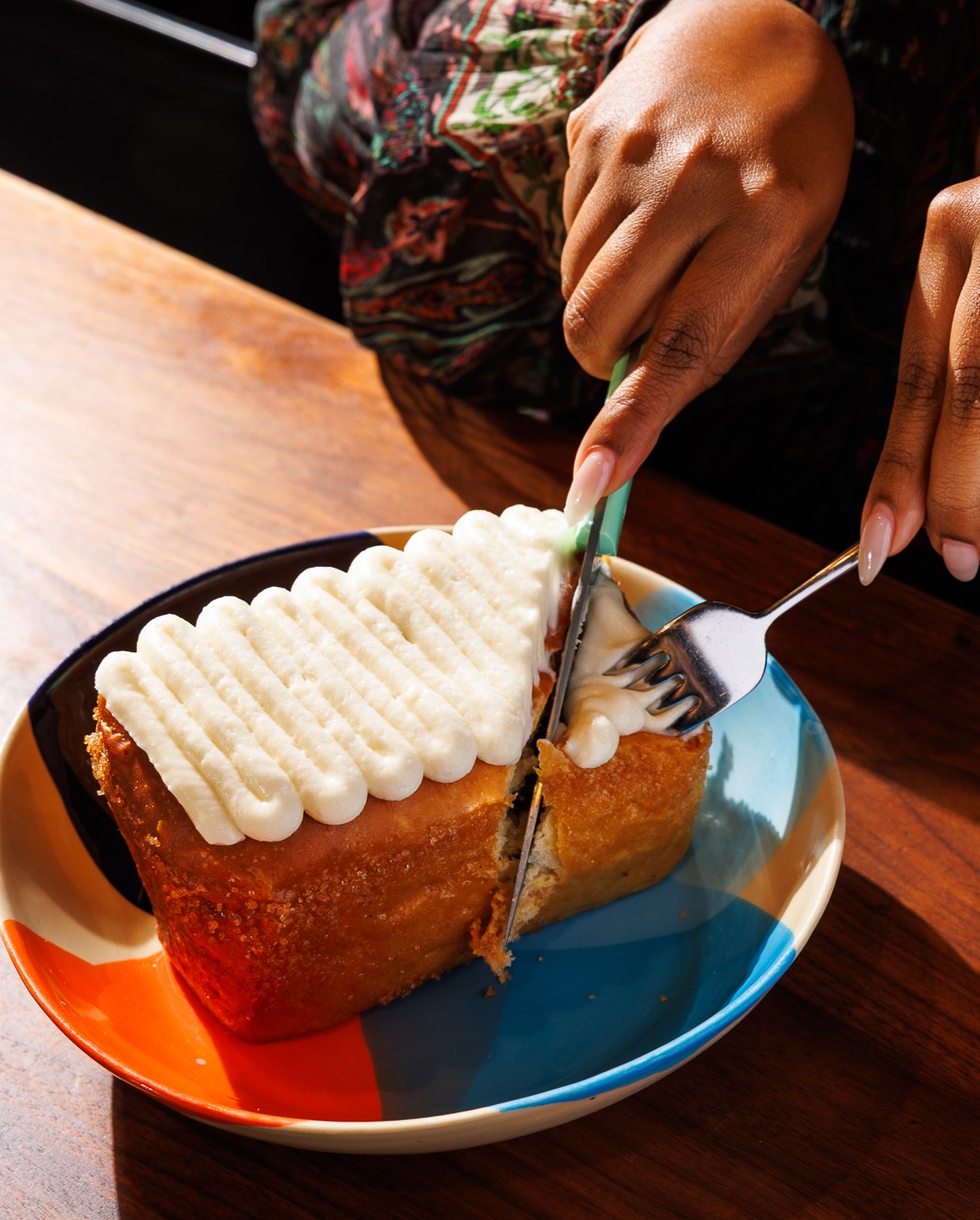 A fluffy coconut turnover is cut into with a knife and fork on top of a blue an orange plate.