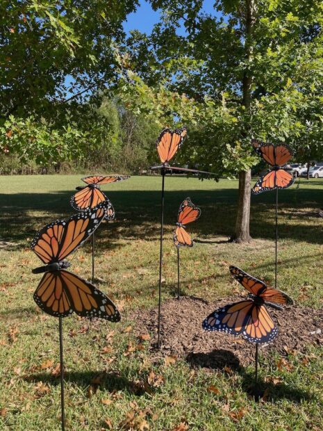 A group of sculptural Monarch butterflies in a park setting.