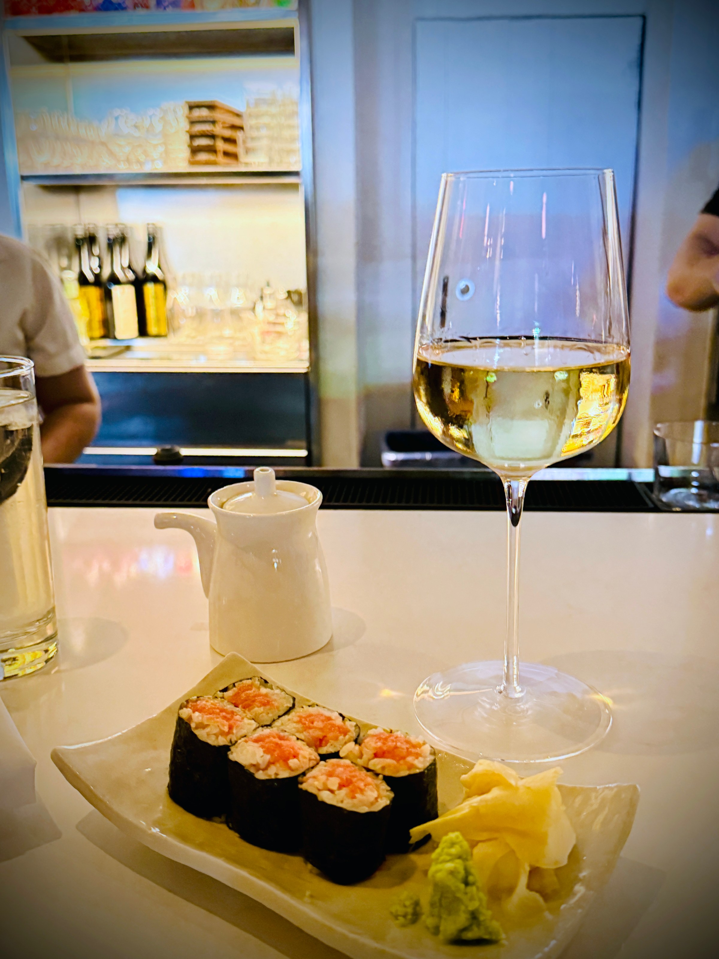 Sushi rolls on a plate with a glass of white wine on a bar counter.
