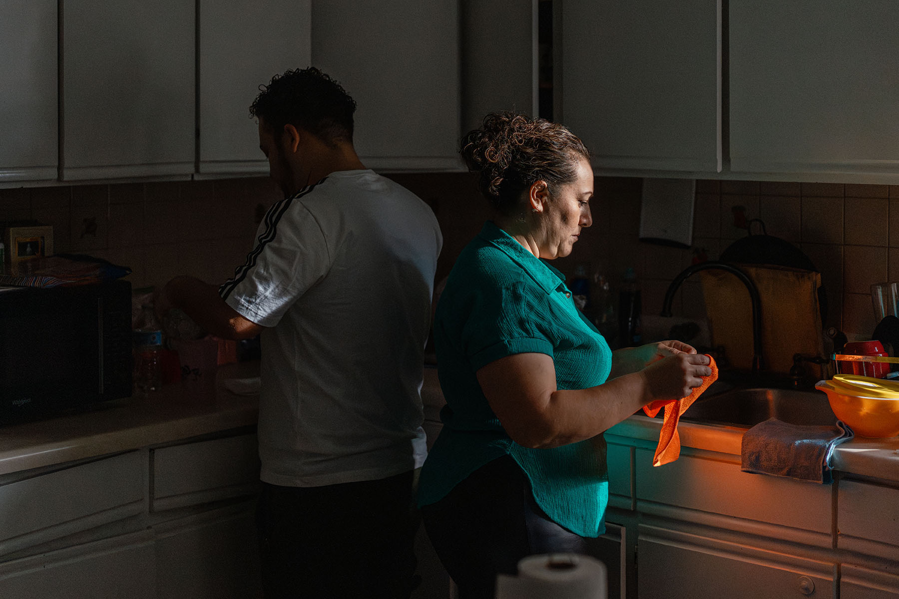 A man and a woman work at the counters in a small kitchen.