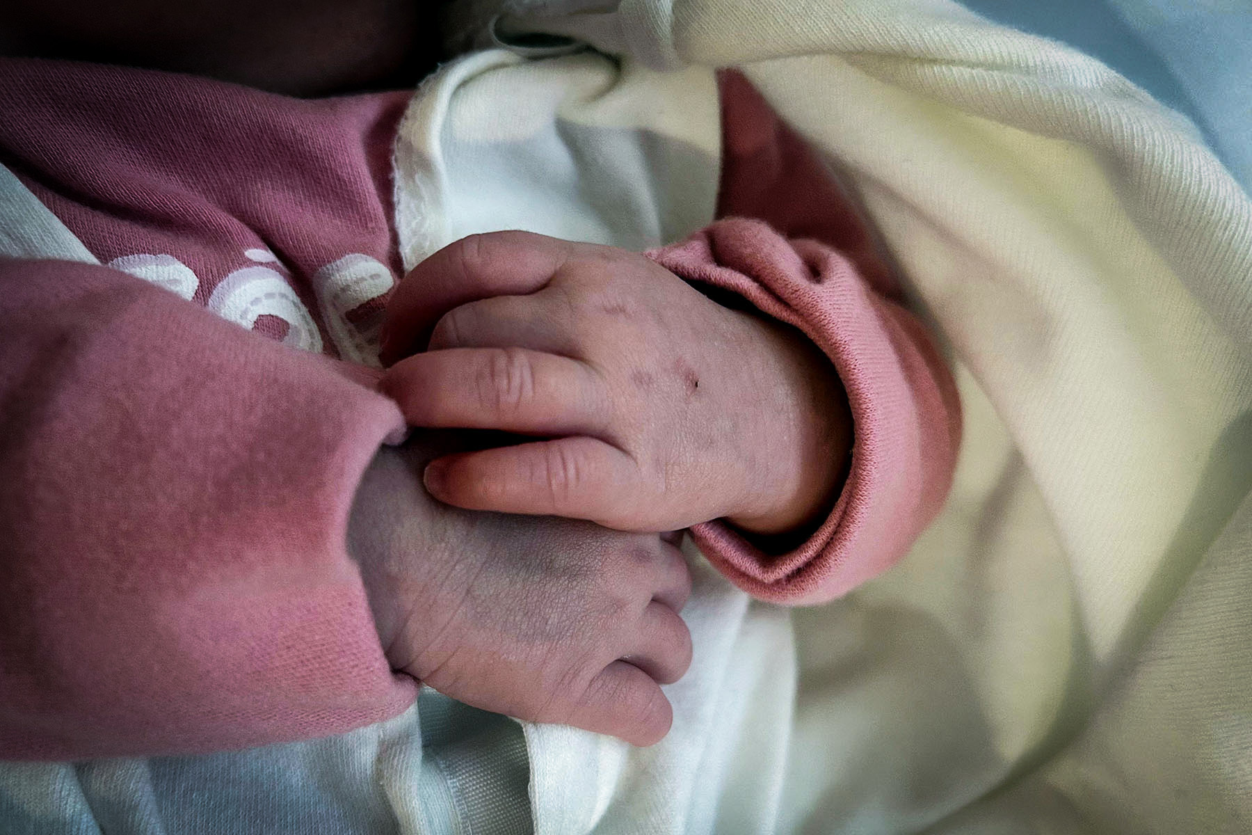 A newborn’s hand in a mitten resting on a blanket in the NICU.