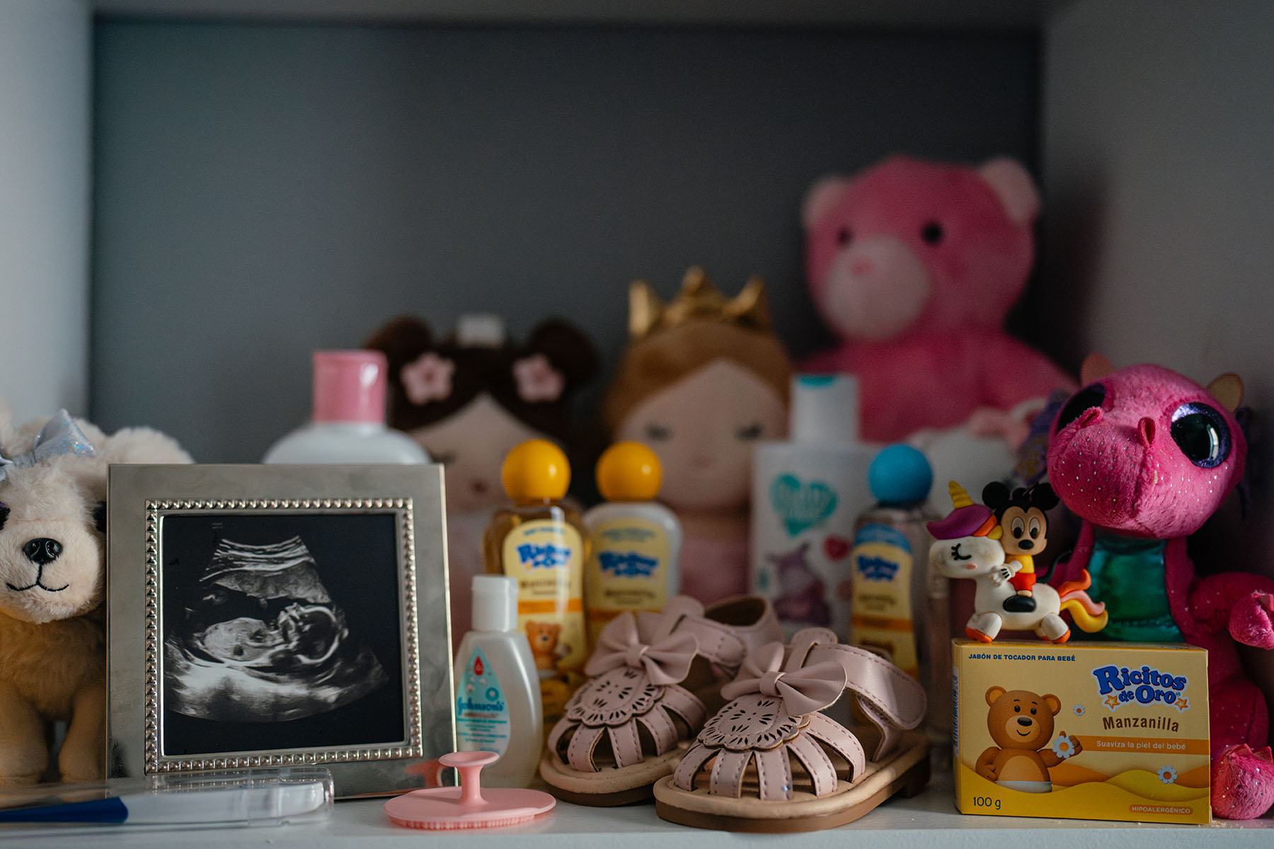 A shelf with baby supplies, toys, and a framed ultrasound photo.
