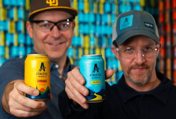 Athletic Brewing Company, Co-Founder and CEO (chief executive officer), Bill Shufelt, left, holds a can of Upside Dawn Golden, and Co-Founder and COO (chief operating officer), John Walker, right, holds a can of Run Wild IPA, at their Miramar facility, Tuesday Nov. 11, 2025, in San Diego, California. Their beers are non-alcoholic with less than 0.5% of alcohol by volume. Howard Lipin / For The San Diego Union-Tribune......NOTE: No sign on the outside of the building, as they're in what used to be the Ballast Point building, which still has the Ballast Point name on it. And not a lot of activity inside.