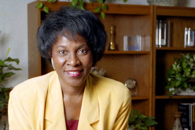 A woman wearing a yellow blazer smiles at a desk in an office.