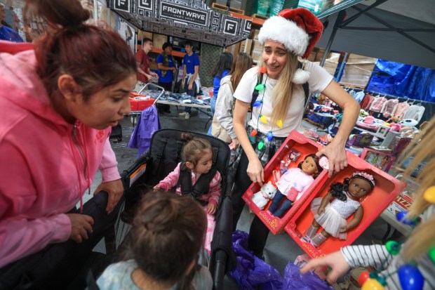 ESCONDIDO, CA - December 13, 2025: Volunteer Robin Kelley shows Lexi Franco, 1, and sister Grace Franco, 4, dolls as they and mother Melissa Franco, left, receive gifts and other items during Interfaith Community Services' annual Winterfaith, a two day event where 250 families in need received food, clothing and Christmas gifts, with the help of around 150 volunteers, at Interfaith Community Services in Escondido on Saturday, December 13, 2025. (Hayne Palmour IV / For The San Diego Union-Tribune)