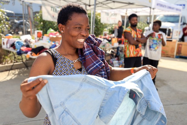 ESCONDIDO, CA - December 13, 2025: Debora Tiakaa, originally from Ghana, smiles as she looks through clothes while she, her husband and son, background, attend the Interfaith Community Services' annual Winterfaith, a two day event where 250 families in need received food, clothing and Christmas gifts, with the help of around 150 volunteers, at Interfaith Community Services in Escondido on Saturday, December 13, 2025. (Hayne Palmour IV / For The San Diego Union-Tribune)