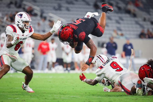 Bert Emanuel Jr. #5 of the San Diego State Aztecs jumps over DaMario Crawford #9 of the Stony Brook Seawolves during the second half at Snapdragon Stadium on Thursday, Aug. 28, 2025 in San Diego, CA. (Meg McLaughlin / The San Diego Union-Tribune)