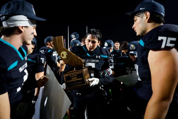 Valley Center's Jesse Morales #6, center, takes a closer look at the trophy after the Jaguars defeated San Jose Lincoln during the Division 6-AA State Championship at Fullerton College on Friday, Dec. 12, 2025 in Fullerton, California. (Meg McLaughlin / The San Diego Union-Tribune)