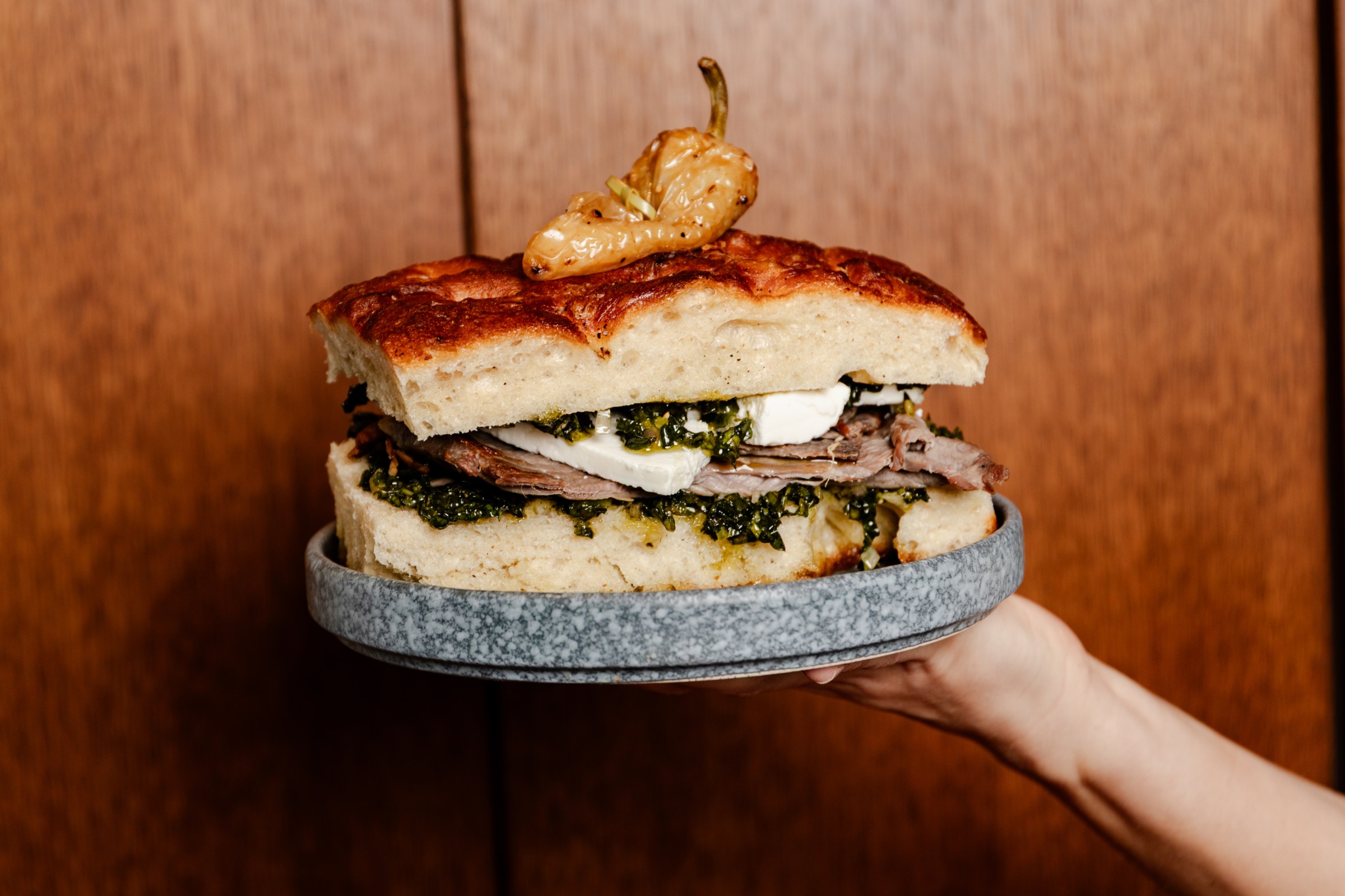 A chef holds up a beef and kale sandwich on a plate.