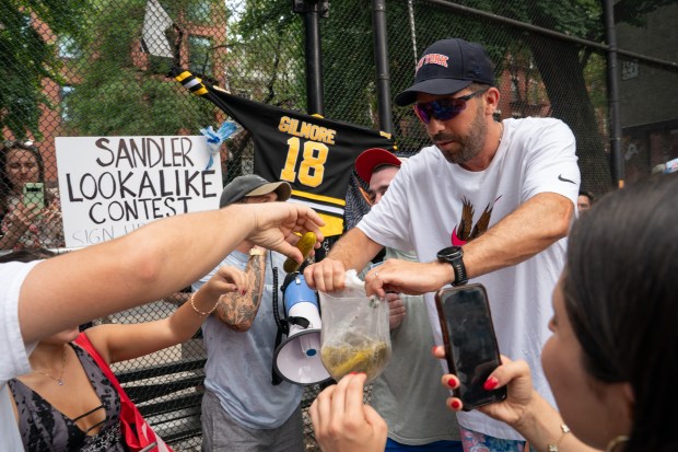 Winner Jason Nagin hands out part of his prize, pickles, after winning an Adam Sandler look a like contest in Vesuvio Playground Friday, June 19, 2025. (Barry Williams/New York Daily News)