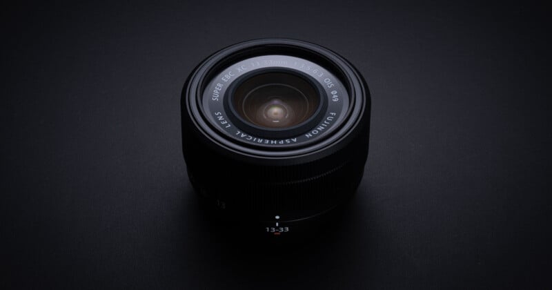 A black camera lens with "Fujinon Aspherical Lens Super EBC XC 16-50mm" written around the rim, photographed from above on a dark surface with soft lighting.