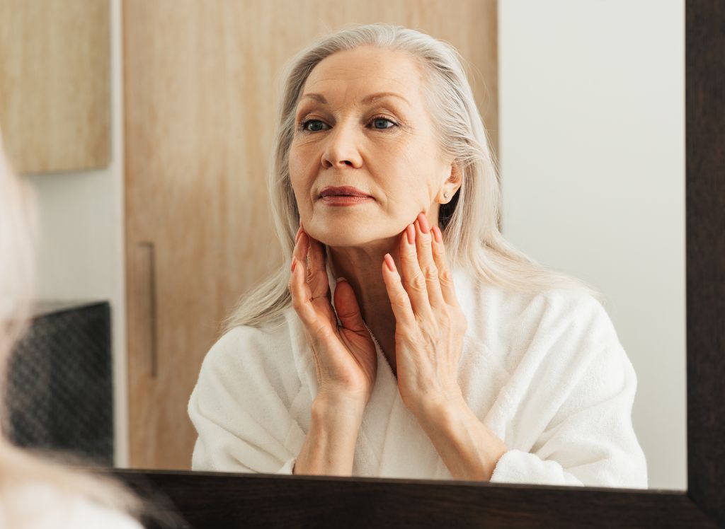  older woman looking at face and neck wrinkles in mirror