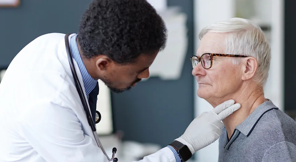 Doctor examines a senior man's throat in a medical office, checking for potential health issues