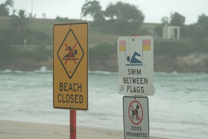 A 'Beach Closed' sign placed in front of choppy waves.