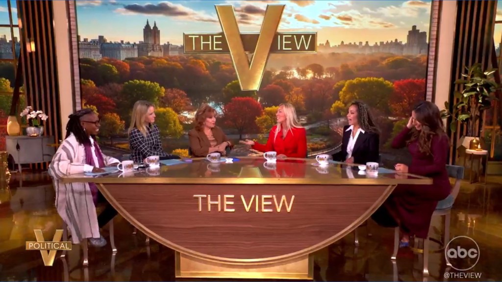 The hosts of "The View" sit around their crescent-shaped table with The View logo behind them.