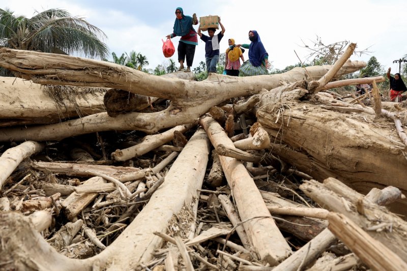 Survivors walk across tree trunks to reach an aid centre in an area affected by a deadly flash flood in Karang Baru, Aceh Tamiang regency, Indonesia, on Dec 6, 2025. (Photo: Reuters)