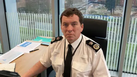 Chief Constable of Merseyside Police Rob Carden sitting at a desk in an office block wearing the shirt from his uniform.
