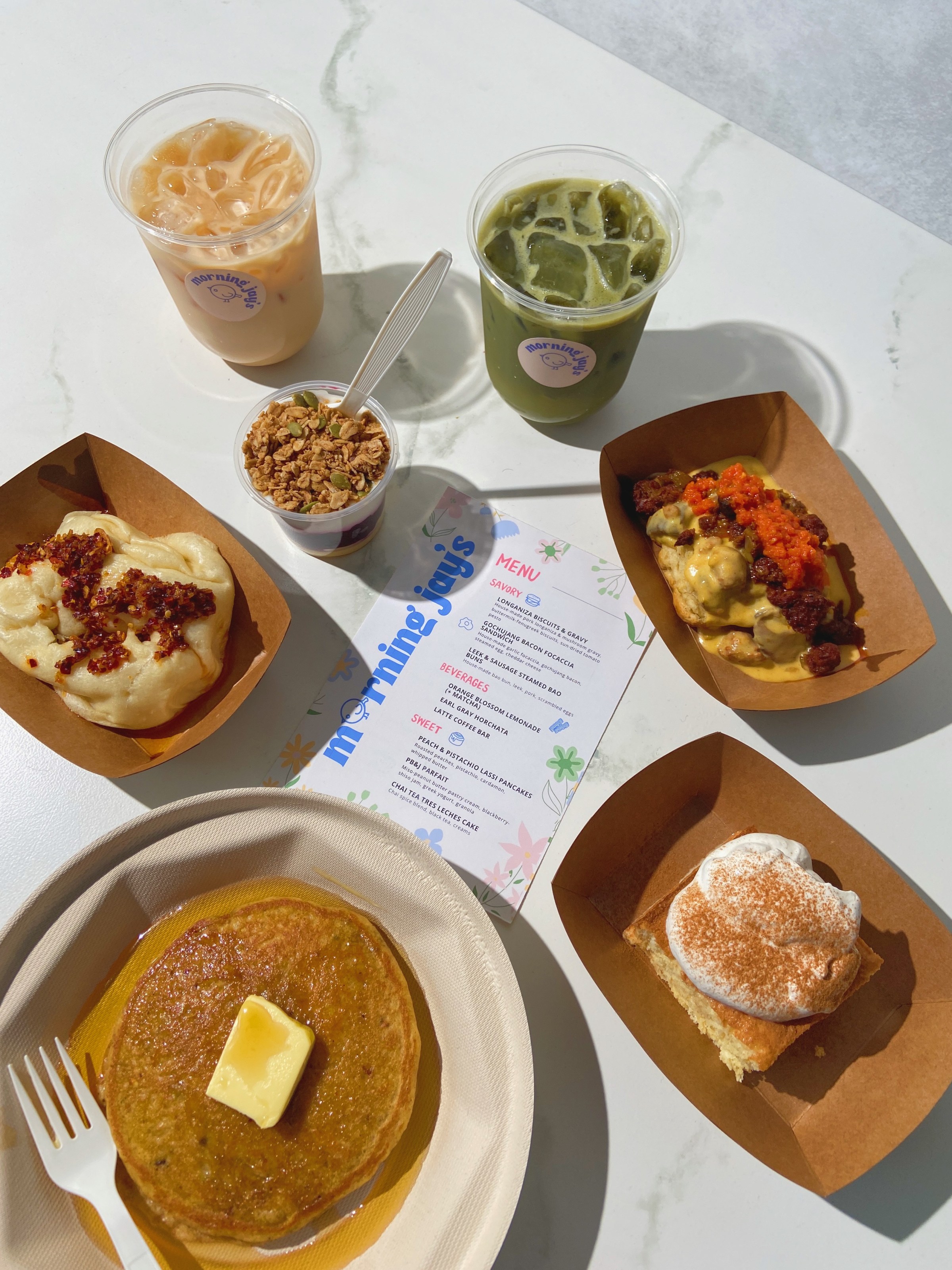 A spread of dishes and drinks surrounding a Morning Jay’s menu.