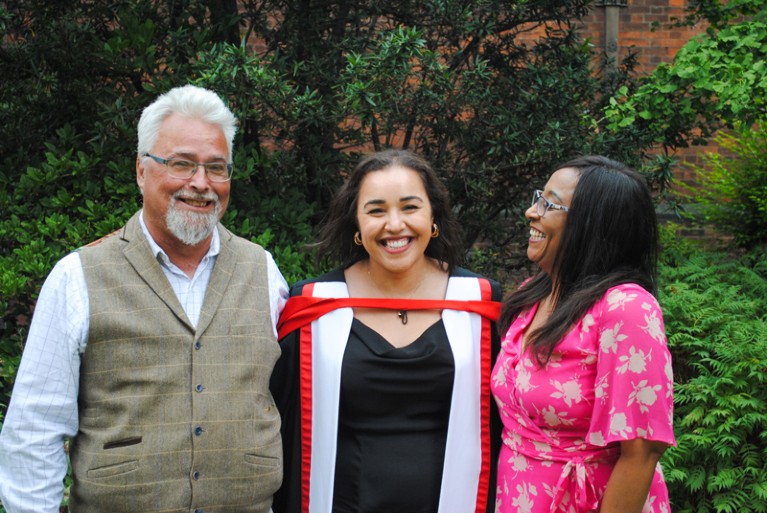 Yasmin Proctor-Kent in a graduation gown with her parents standing on either side of her