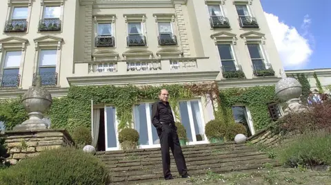 Hulton Archive/Getty Images A man dressed in black stands on steps in front of a smart house