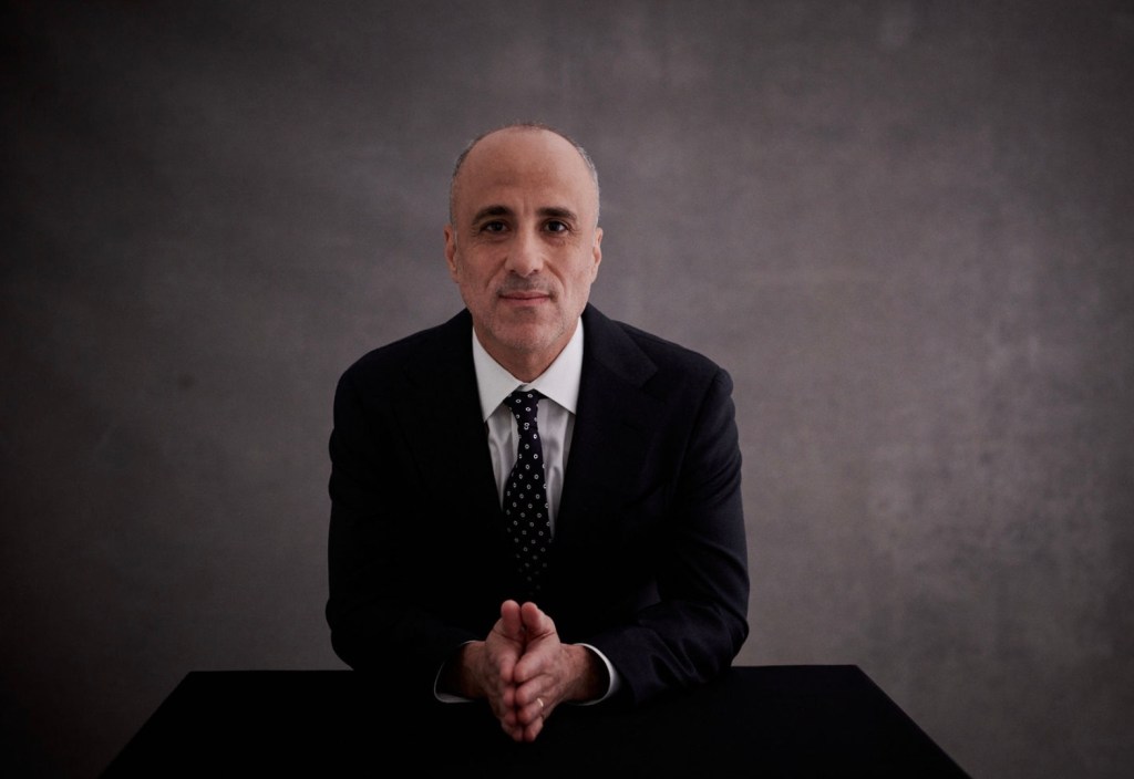 Drew Warshaw, candidate for NY State Comptroller, sitting at a table with hands clasped.