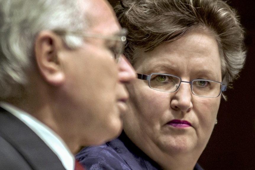 A man who is slightly blurred standing in front of a woman who is looking towards him in front of a microphone