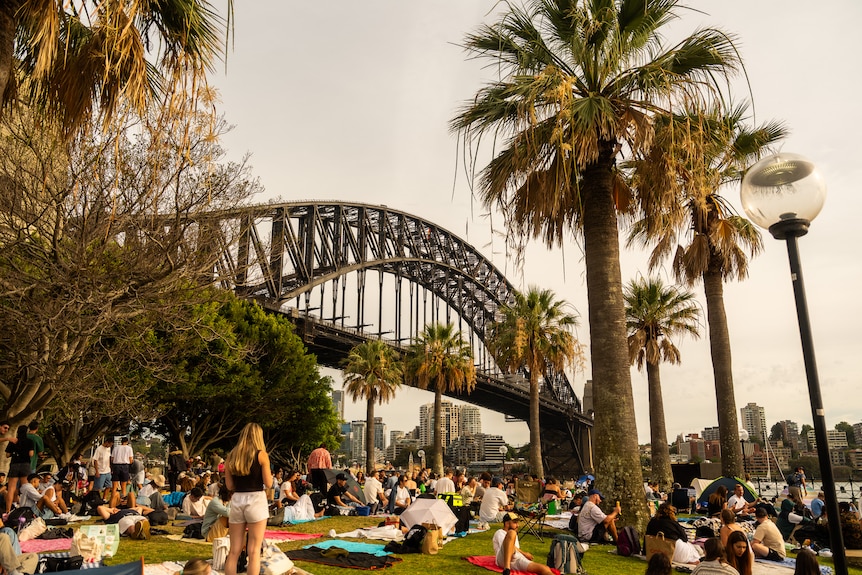 A crowd of people sitting in front of the Sydney Harbour Bridge.