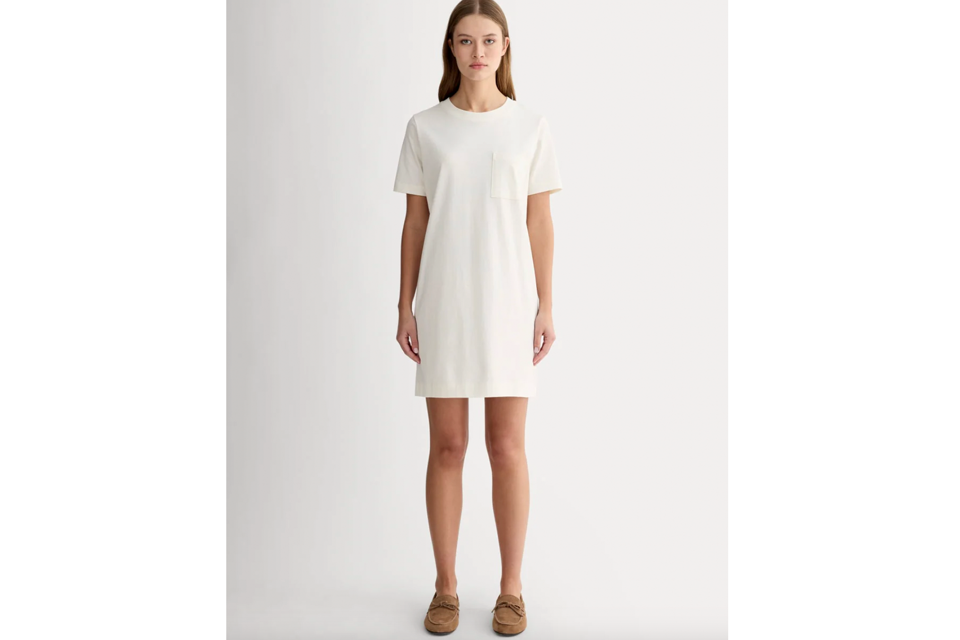 A woman stands facing forward, wearing a white t-shirt dress and brown boat shoes.