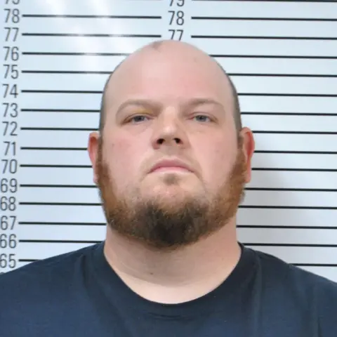 Stephens County Sheriff's Office A police booking photo of Cody Wayne Adams, who is bald with a beard, and in a blue T-shirt