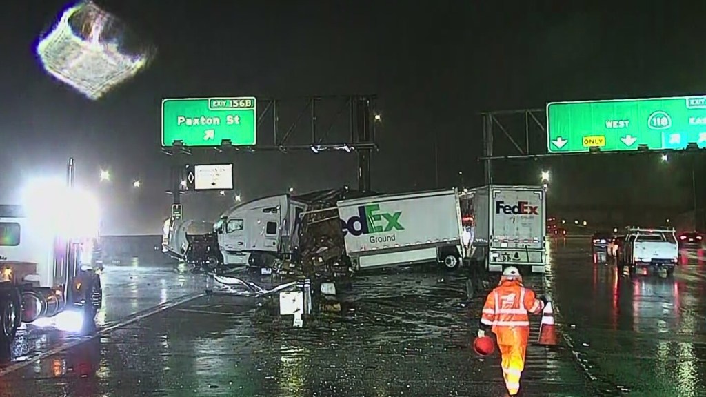 A FedEx truck crash on a highway at night, with a worker in an orange jumpsuit.