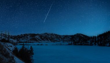 A shooting star is pictured streaking down through a starry sky above a frozen lake it night, bordered by snow-dappled hills.