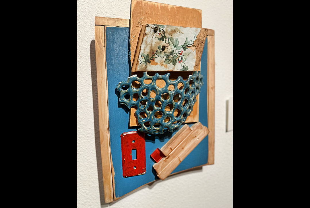 An abstracted sculpture made of found materials hanging on the wall.