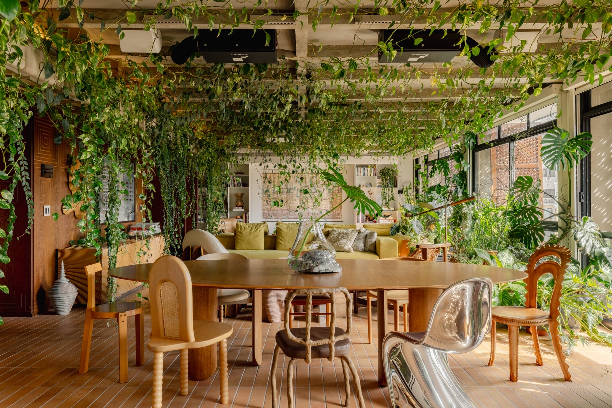 An apartment interior designed by Guto Requena with an eclectic variety of contemporary furnishings and houseplants draping from rafters in the ceiling